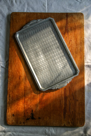 old wooden board on a white linen tablecloth and a metal rectangular tray lace towel sunny natural...