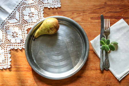 Vintage silverware and metal round plate on a white linen napkin on a rustic wooden background and lace towel. Top view of natural sunlight, shadows. Beautiful background, mockup with empty space.の写真素材