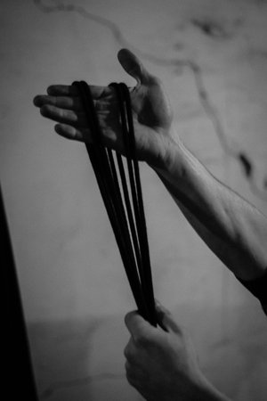 A man holds black shibari ropes in his hand, winds and ties. black and white photo