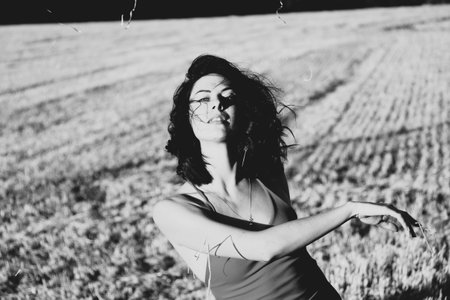Portrait of a young beautiful brunette in a dress against the background of a mown wheat field, in the summer outdoors, sunset light. Woman happy dancing, black and white photoの写真素材