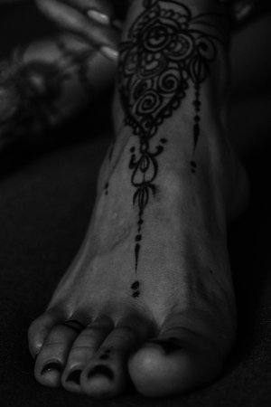 Close-up of female legs and hands with henna tattoo on the feet. Black and white photo. Gently feminine graceful decoration, respect for a woman, love and take care of yourself.の写真素材