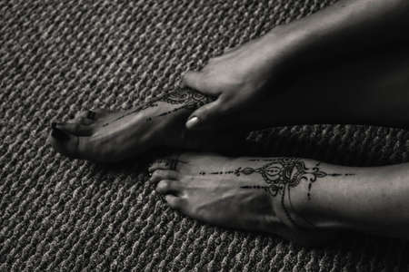 Close-up of female legs and hands with henna tattoo on the feet. Black and white photo. Gently feminine graceful decoration, respect for a woman, love and take care of yourself.の写真素材