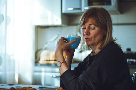Portrait of an attractive adult woman, cute smiling, holding a mug in the home kitchen. quiet breakfast at home alone. Natural daylight.の写真素材
