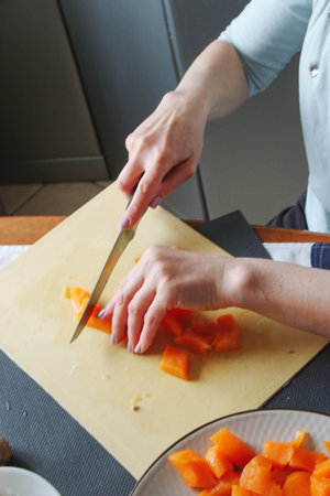 Close-up female adult hands cut orange pumpkin, prepare food in her home kitchen, ordinary household real process natural light, selective sharpness.の写真素材