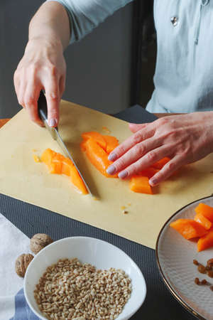 Close-up female adult hands cut orange pumpkin, prepare food in her home kitchen, ordinary household real process natural light, selective sharpness.の写真素材