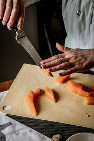 Close-up female adult hands cut orange pumpkin, prepare food in her home kitchen, ordinary household real process natural light, selective sharpness.の写真素材