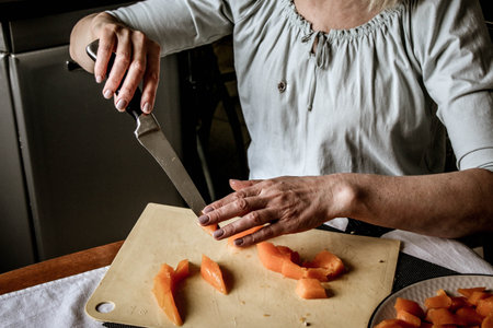 Close-up female adult hands cut orange pumpkin, prepare food in her home kitchen, ordinary household real process natural light, selective sharpness.の写真素材