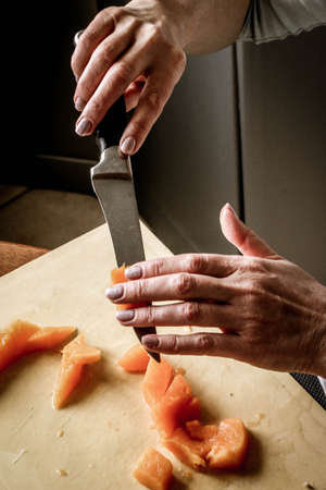 Close-up female adult hands cut orange pumpkin, prepare food in her home kitchen, ordinary household real process natural light, selective sharpness.の写真素材
