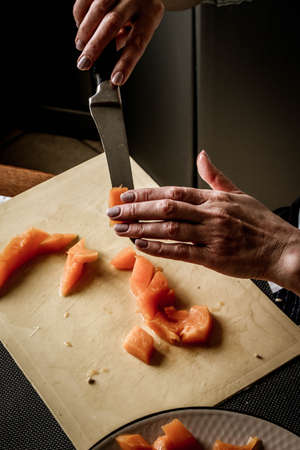 Close-up female adult hands cut orange pumpkin, prepare food in her home kitchen, ordinary household real process natural light, selective sharpness.の写真素材