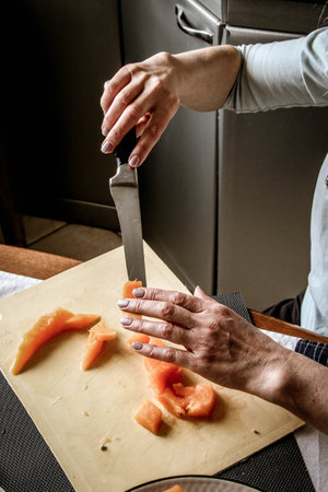 Close-up female adult hands cut orange pumpkin, prepare food in her home kitchen, ordinary household real process natural light, selective sharpness.の写真素材
