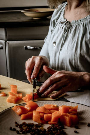 Close-up female adult hands cut orange pumpkin, prepare food in her home kitchen, ordinary household real process natural light, selective sharpness.の写真素材