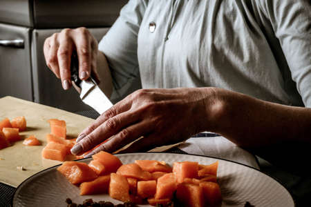 Close-up female adult hands cut orange pumpkin, prepare food in her home kitchen, ordinary household real process natural light, selective sharpness.の写真素材