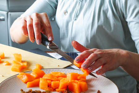 Close-up female adult hands cut orange pumpkin, prepare food in her home kitchen, ordinary household real process natural light, selective sharpness.の写真素材
