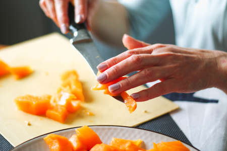 Close-up female adult hands cut orange pumpkin, prepare food in her home kitchen, ordinary household real process natural light, selective sharpness.の写真素材
