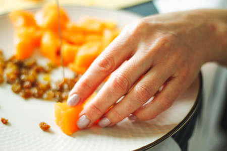 Close-up female adult hands cut orange pumpkin, prepare food in her home kitchen, ordinary household real process natural light, selective sharpness.の写真素材