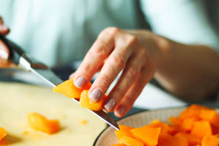 Close-up female adult hands cut orange pumpkin, prepare food in her home kitchen, ordinary household real process natural light, selective sharpness.の写真素材