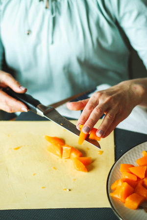 Close-up female adult hands cut orange pumpkin, prepare food in her home kitchen, ordinary household real process natural light, selective sharpness.の写真素材