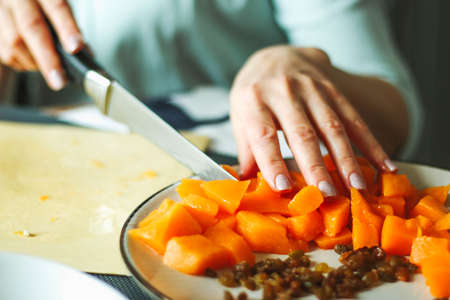 Close-up female adult hands cut orange pumpkin, prepare food in her home kitchen, ordinary household real process natural light, selective sharpness.の写真素材