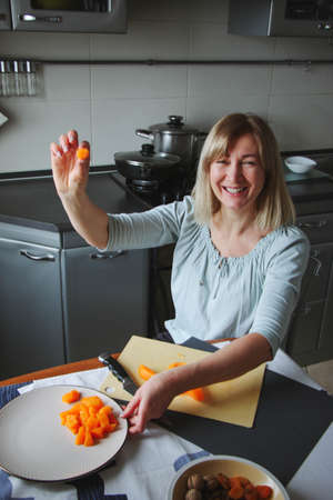 An adult woman, blonde, calmly prepares food in the home kitchen, shifts the tuuva, touches the food, looks to the side or to the camera. A simple household process in natural light.の写真素材