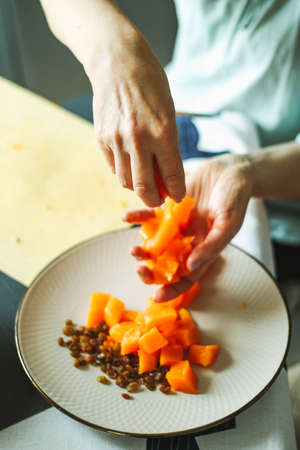 Close-up female adults shift touch orange pumpkin and raisins, prepare food in their home kitchen, normal home natural light process, selective sharpening.の写真素材