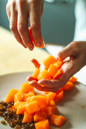 Close-up female adults shift touch orange pumpkin and raisins, prepare food in their home kitchen, normal home natural light process, selective sharpening.の写真素材