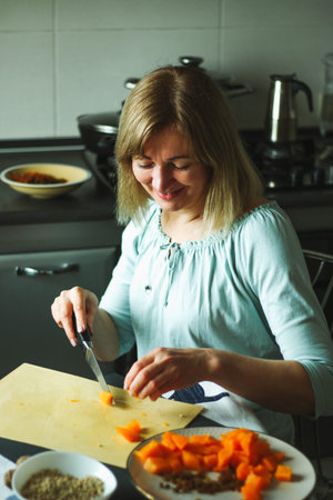 An adult woman, blonde, calmly prepares food in the home kitchen, shifts the tuuva, touches the food, looks to the side or to the camera. A simple household process in natural light.の写真素材