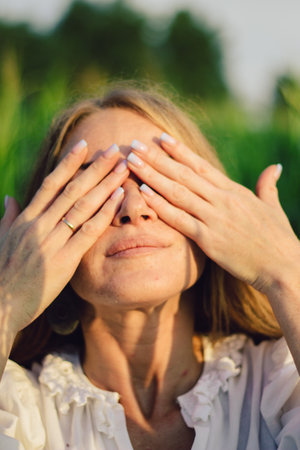 Young beautiful woman with long red hair between green leaves on a corn field in summer, in the light of the setting sun.の写真素材