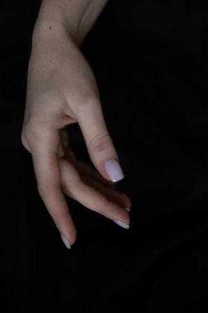 Close-up of a beautiful female hand with a simple nail manicure, on a gray background, selective focus. Weave long fingers and a fragile wrist, plastic movement.の写真素材