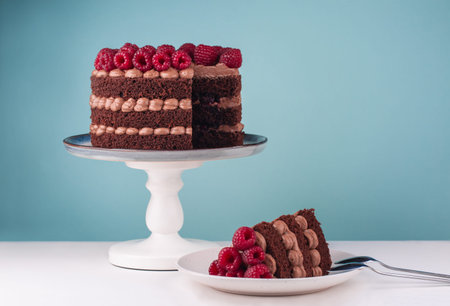 Chocolate birthday cake with raspberries and butter cream on  white table and blue background. Piece...