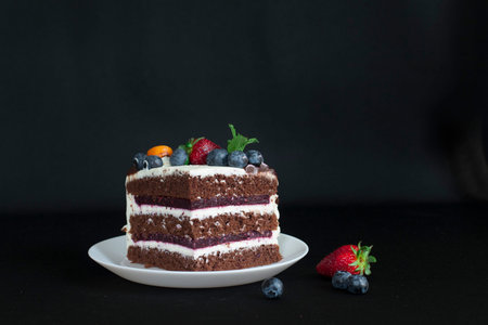 Layered chocolate cake decorated with flowers and berries on the garden table.