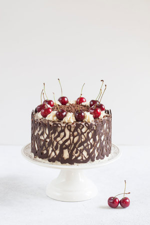 German cake - Black forest, with chocolate decoration and cherries. On white table with white...