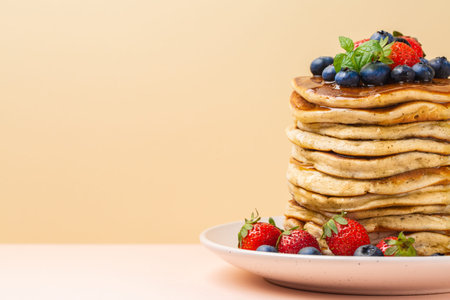 A stack of pancakes with honey, strawberries and blueberries. Copy space, text box. Peach and pink...