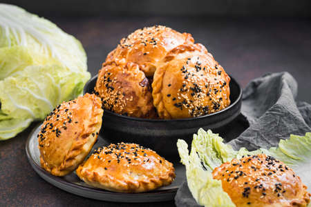 Samosa - baked pastry with a savoury filling: meat, onion and napa cabbage. Homemade, round shape, with sesame seeds. Grey background..の写真素材