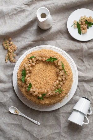 Homemade Medovik cake - a Russian layer cake with honey, decorated with white currants. On the table with linen tablecloth. Top view. Natural color.の写真素材