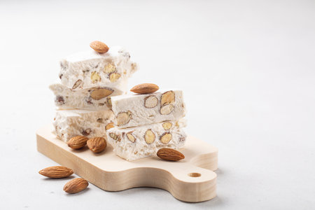 Torrone - soft italian nougat with almonds. On small wood board. White background. Copy space.の写真素材
