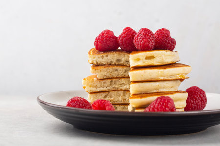 Cuted stack of fluffy pancakes with raspberries. On light table and white background. Close-up. Copy...