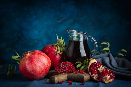 Pomegranate juice in a jug, whole pomegranates and seeds on dark blue background. Dark and moody.の写真素材