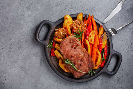 Dinner with beef steak and baked vegetables, pototoes, carrots, bell peppers, garlic with rosemary. Flat lay, grey background, copy space.の写真素材
