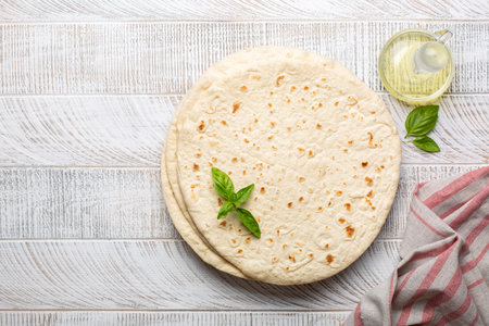 Italian flatbread - piadina Romagnola. Olive oil, basil leaves. White wood background.
