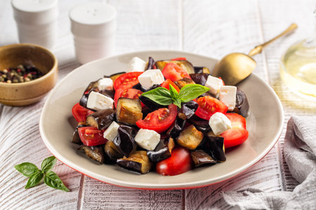 Summer salad with feta cheese, baked eggplant and fresh tomatoes, basil, olive oil. Light background.の写真素材