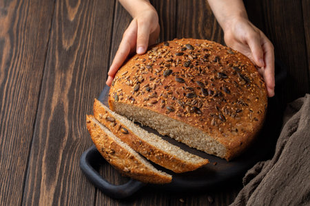Girl's hands holding home baked bread with whole wheat bread  and different seeds. Long leavened,...