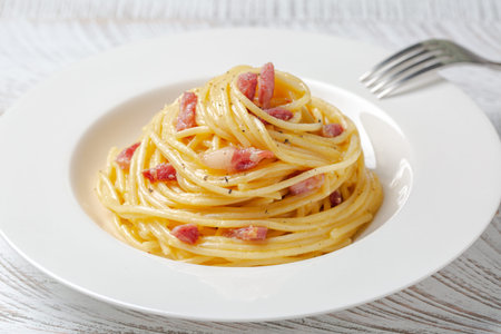 Spaghetti carbonara in a white plate. Spaghetti, pancetta and sauce made of egg yolk and parmesan cheese, black pepper. Close-up.の写真素材