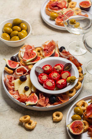 Traditional italian aperitivo, snacks and vermouth cocktail. Bruschetta, cold cuts of prosciutto, cheese, tuna fish stuffed mini bell peppers, taralli, olives, grapes and figs. Vertical image.の写真素材