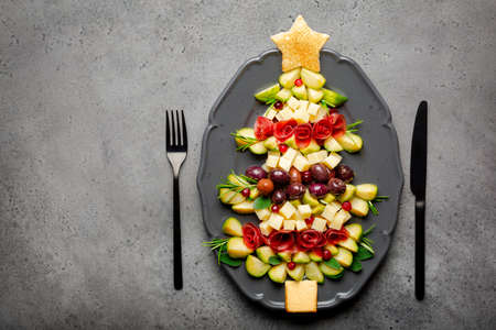 Christmas tree shape appetizers board: cheese, olives, brussels sprout, beef cold cuts, toast bread, sage, rosemary. Festive dinner idea, grey background, copy space.の写真素材