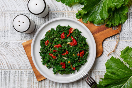 Cooked turnip greens with garlic and tomatoes. The dark leafy edible green tops of turnips. They are high in nutrients and low in calories. On white wood table surface.の写真素材