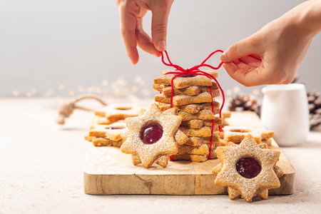 Preparing a cookie gift. Girls hands tying a red cotton bow cord. Homemade star or flower shaped...