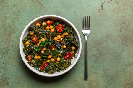 Sauteed kale, sun-dried tomato and chickpea salad.  Vegetarian dish. Green table surface. Top view.