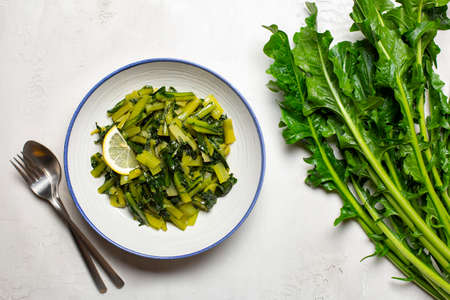 Sauteed chicory greens with olive oil and lemon and fresh head of chicory on white table.の写真素材