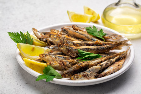 Close up of pan-fried anchovies in the white plate with lemon and parsley. White background.の写真素材