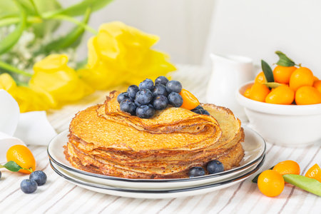 Stack of sweet crepes,  type of pancake, with blueberry and kumquat. Festive breakfast. Yellow...